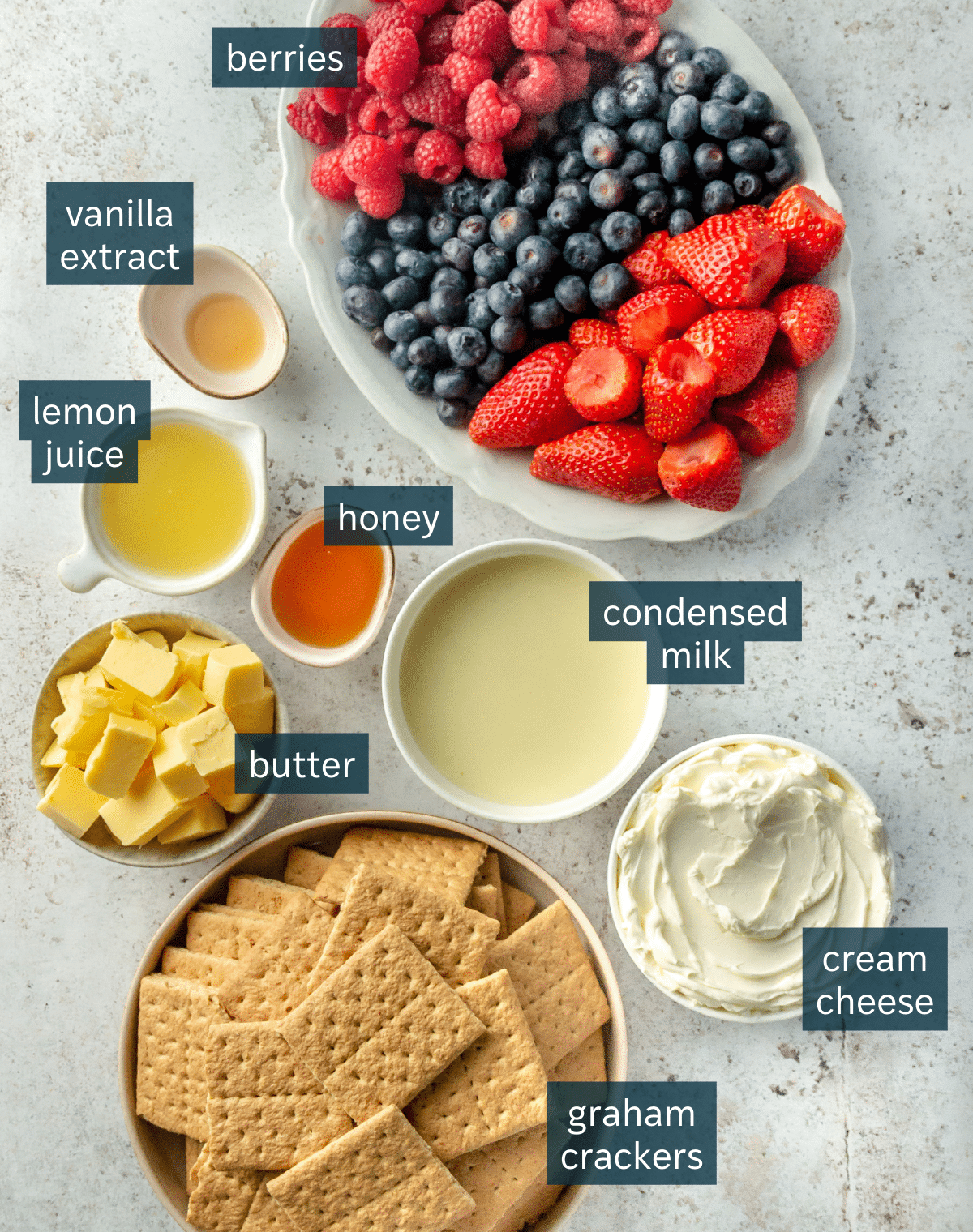 All of the ingredients needed for no-bake mason jar cheesecakes in different sized bowls and plates on a light gray surface.