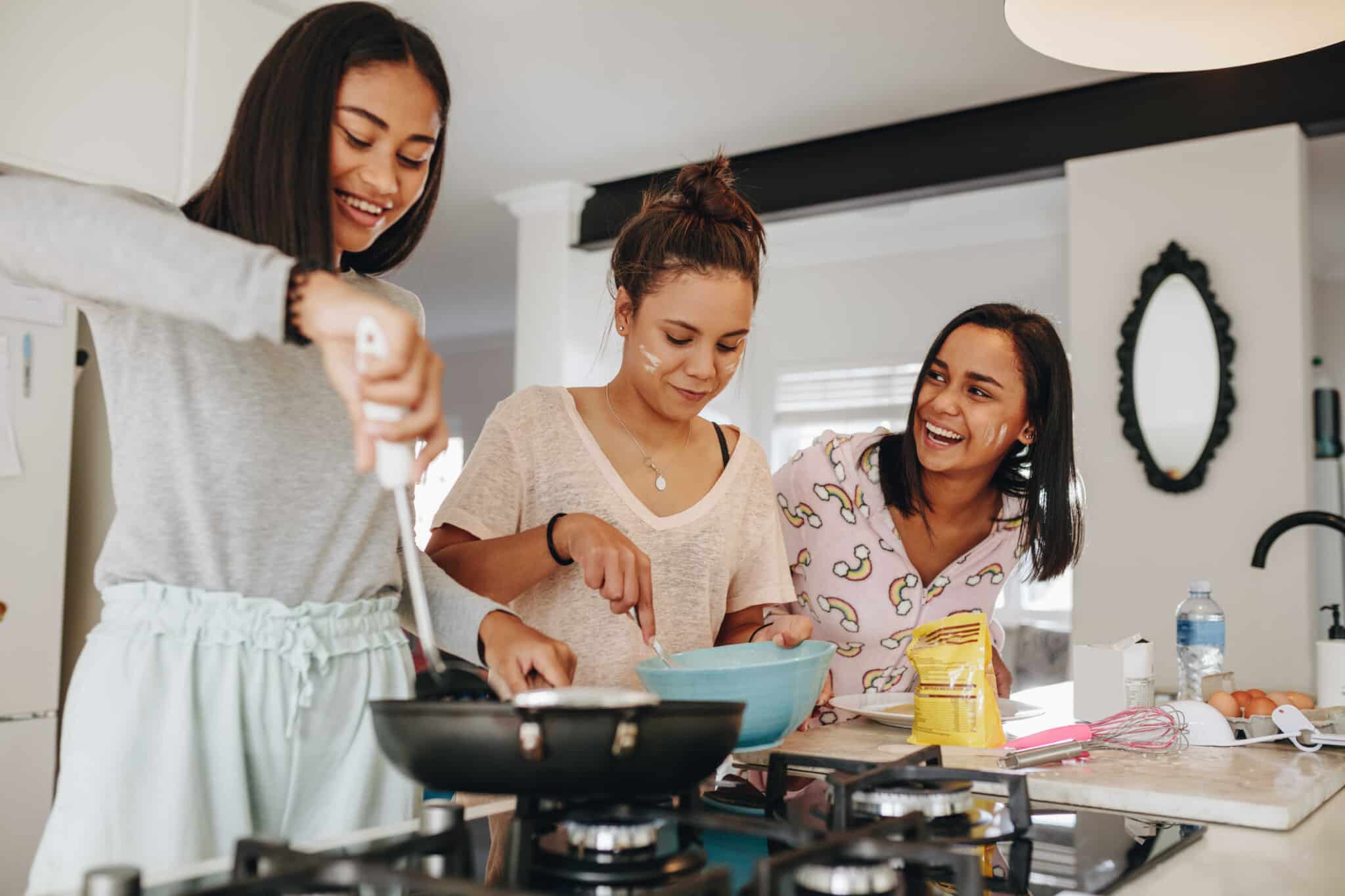 3 teenage girls smiling and cooking on the stovetop