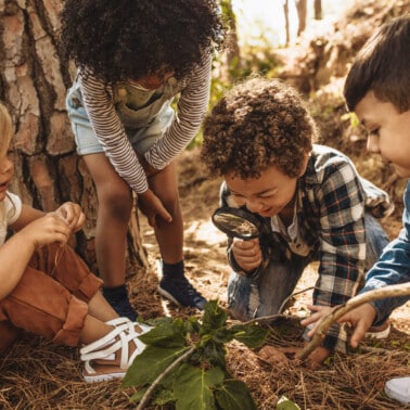 four kids exploring nature, one boy holding a magnifying glass