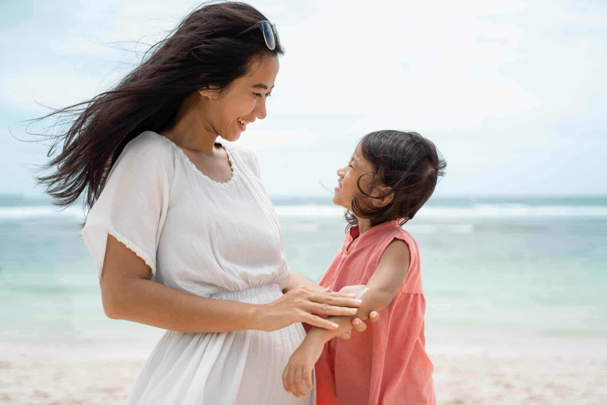 mother rub a sunblock to daughter's skin on the seashore at midday