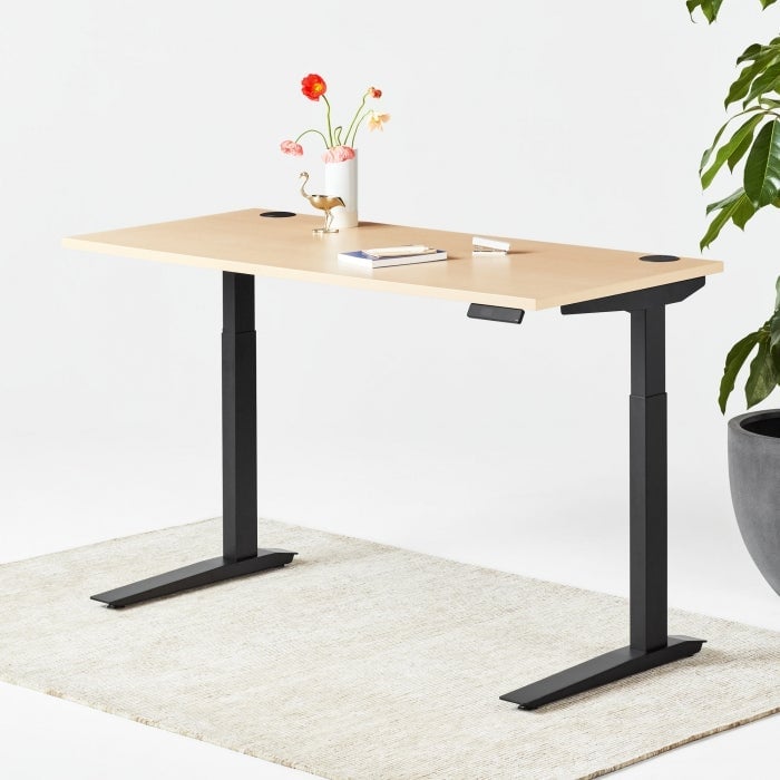 a black and wood standing desk with a vase of flowers on it