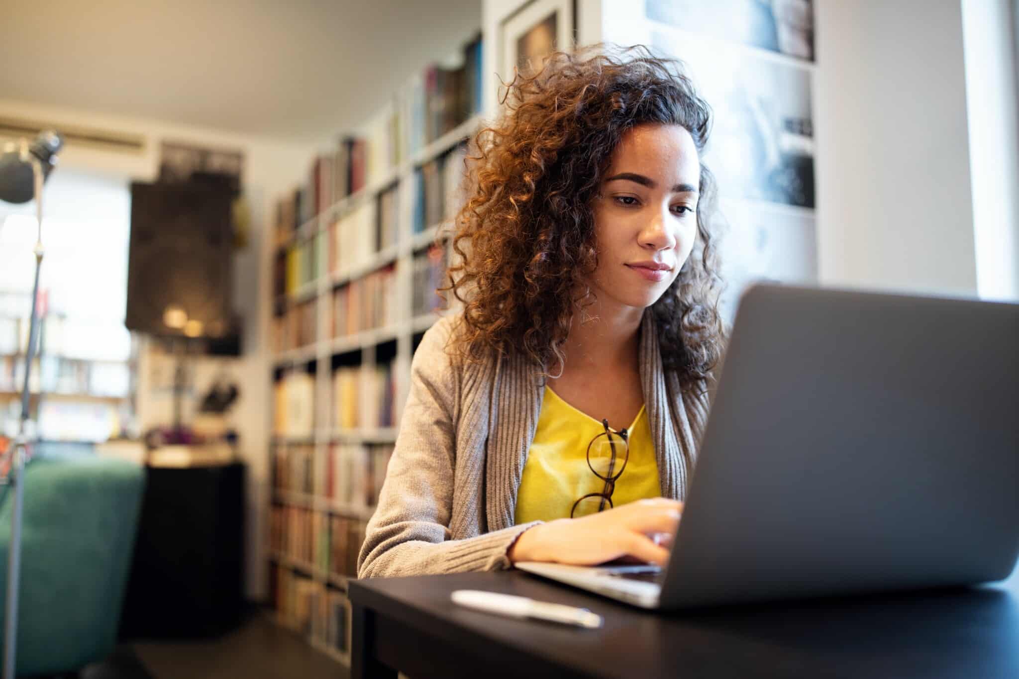 woman working at her laptop with bookshelves in the background