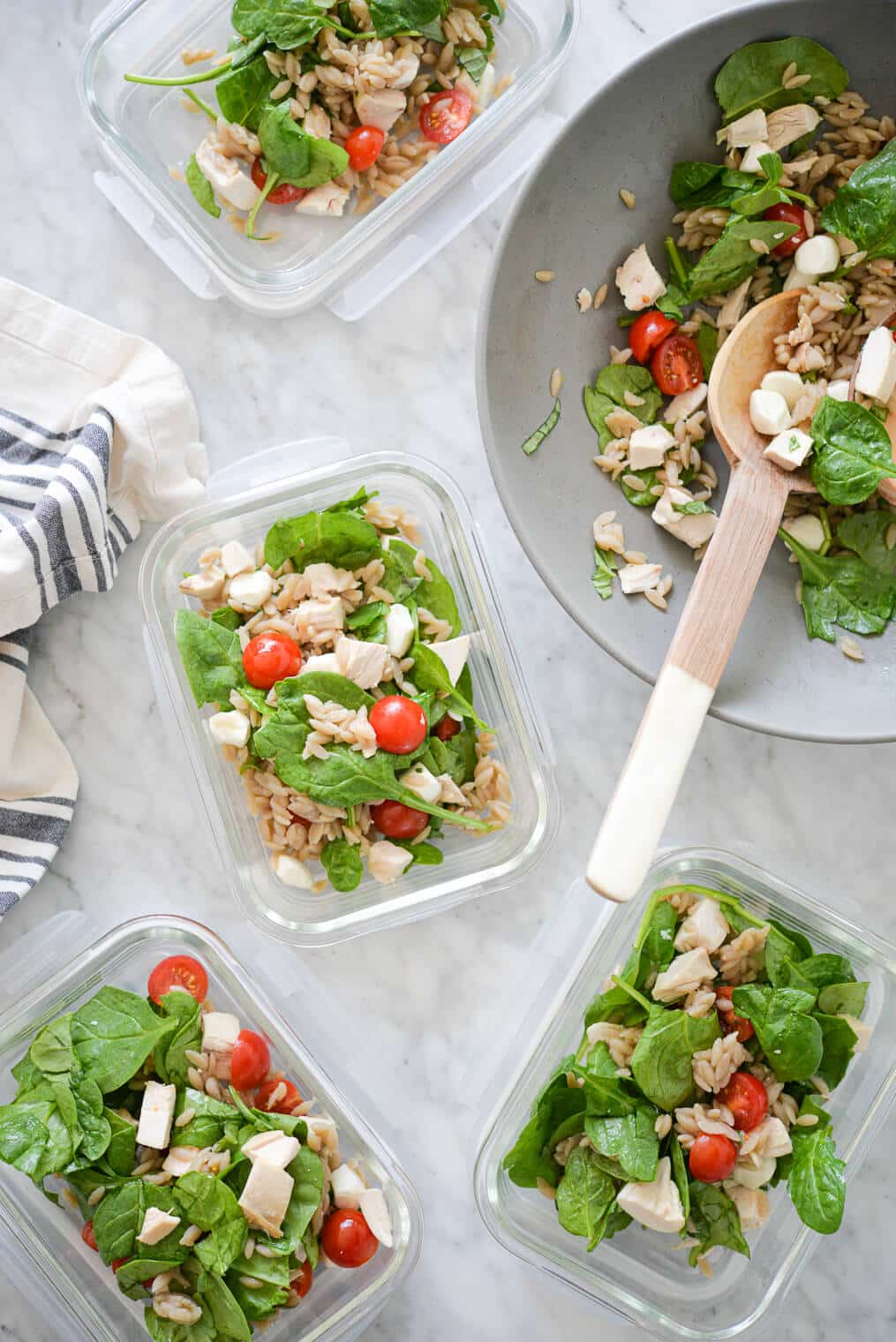 a large bowl of orzo caprese salad being split among smaller glass meal prep containers