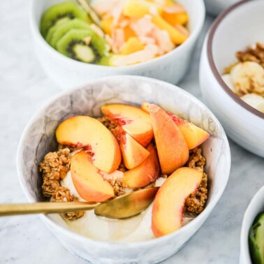 top view of a marble bowl with plain Greek yogurt, sliced fresh peaches, granola, and honey on a marble surface