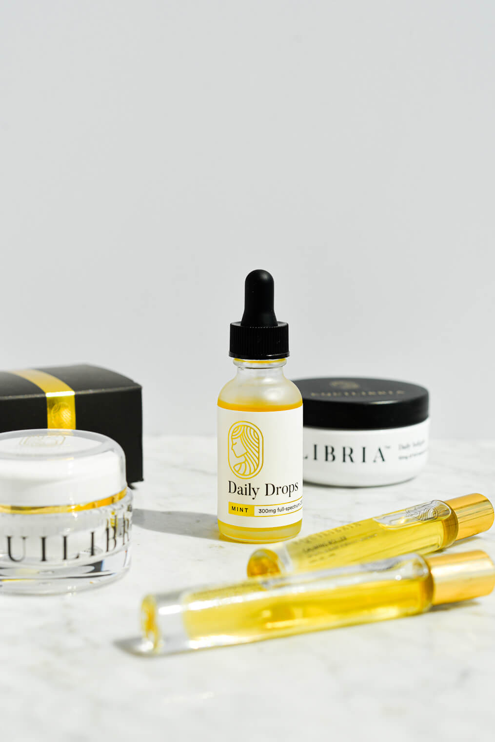 a glass bottle of equilibria cbd drops, rollers, relief cream, and softgels on a marble surface