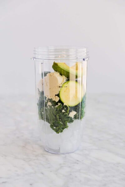 ingredients for green smoothies in an individual serving blender cup sitting on a marble surface