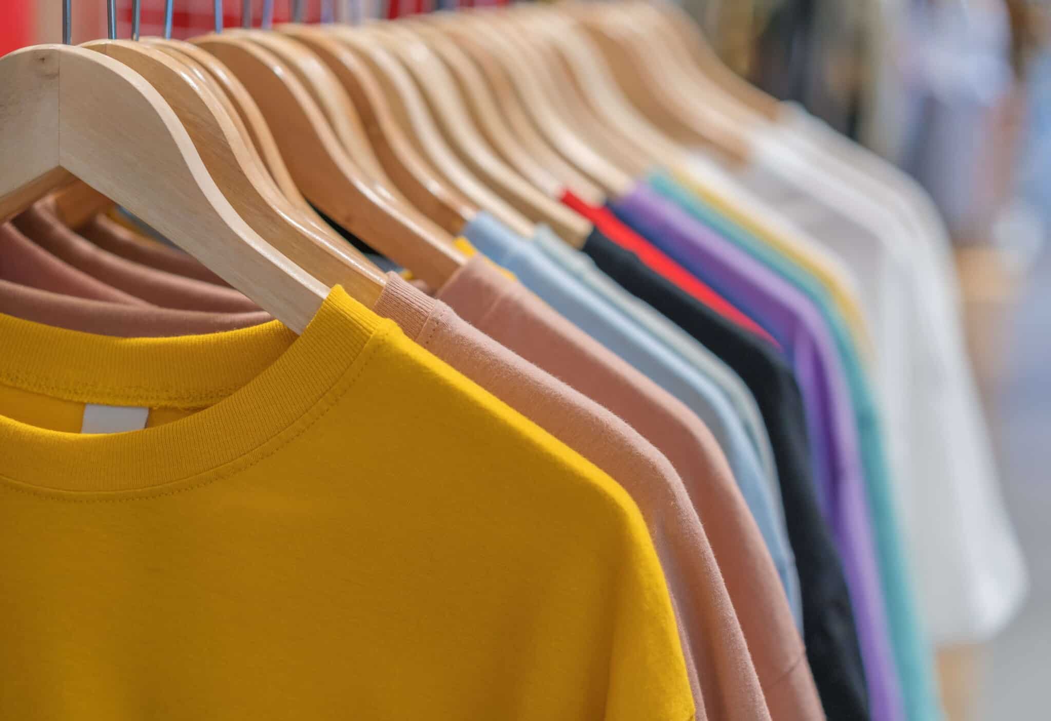 multiple colors of tshirts hanging on wooden hangers on a rack