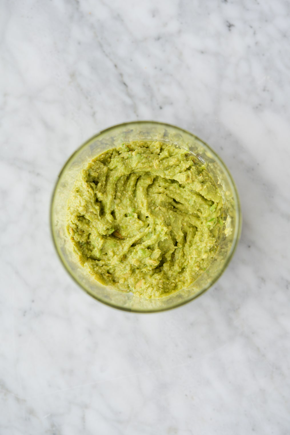 mashed avocado and oatmeal soothing face mask in a glass jar on a marble surface