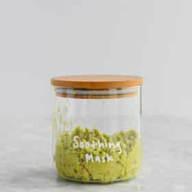 mashed avocado and oat mask in a glass jar with a wooden lid with soothing mask written on it in white letters on a marble surface