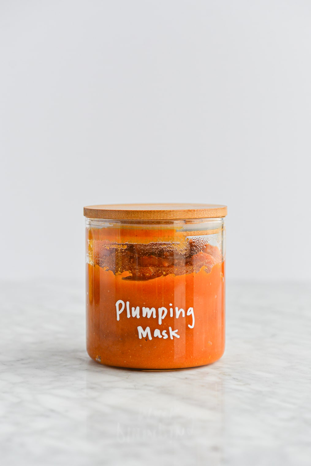 homemade pumpkin mask in a glass jar with a wooden lid with plumping mask written on it in white letters on a marble surface