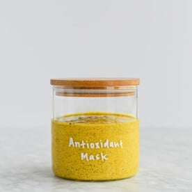 bright yellow turmeric and yogurt face mask in a glass jar with a wooden lid with the words 'antioxidant mask' written in white lettering