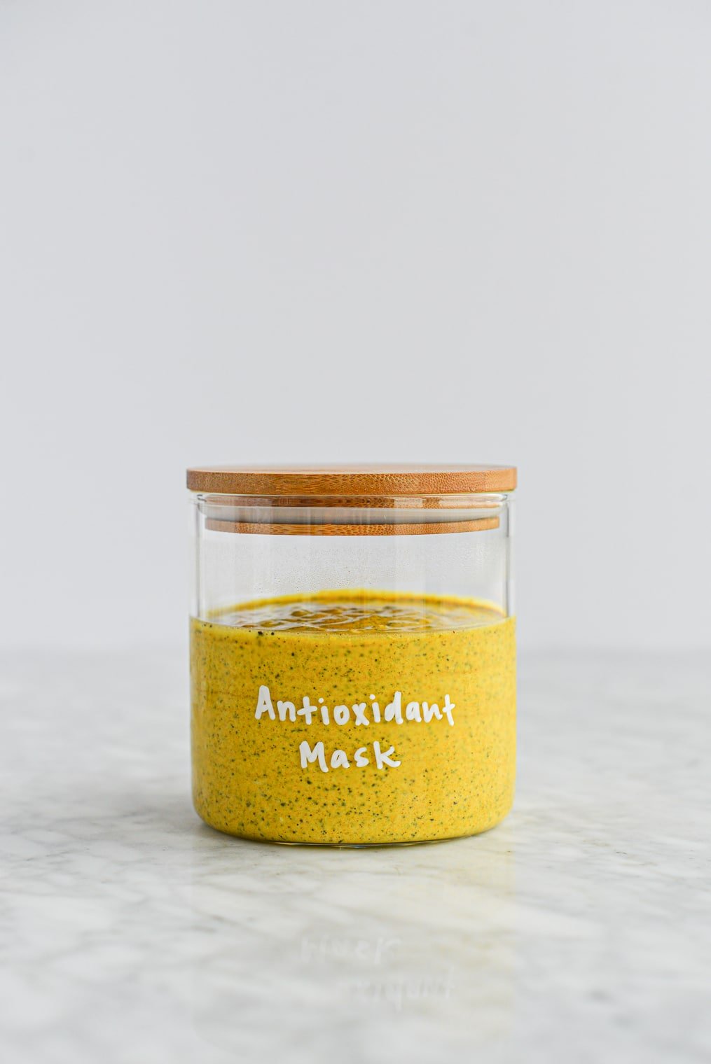 bright yellow turmeric and yogurt face mask in a glass jar with a wooden lid with the words 'antioxidant mask' written in white lettering