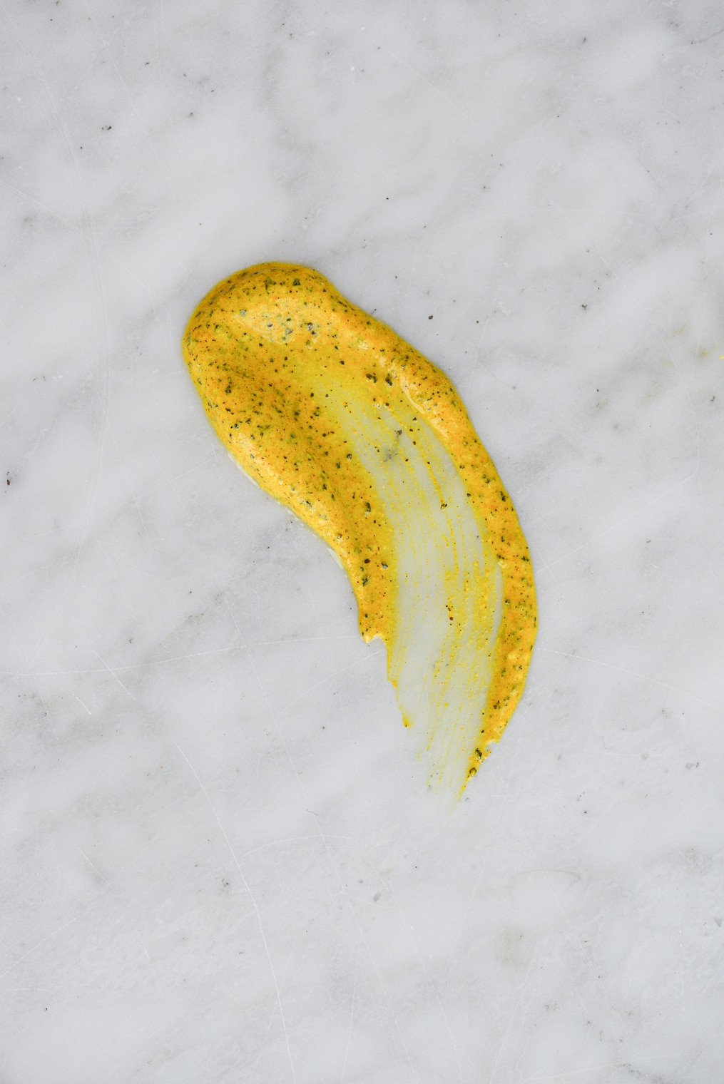 bright yellow yogurt and turmeric mask with black speckles smeared on a marble surface