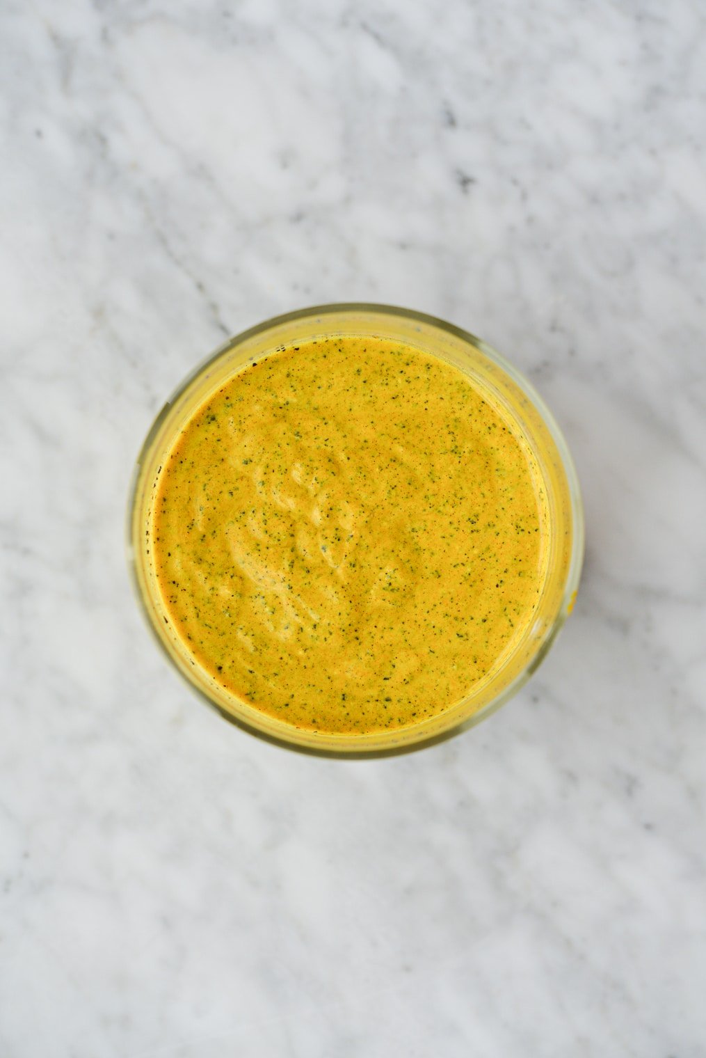 overhead shot of a bright yellow turmeric face mask in a glass jar on a marble surface