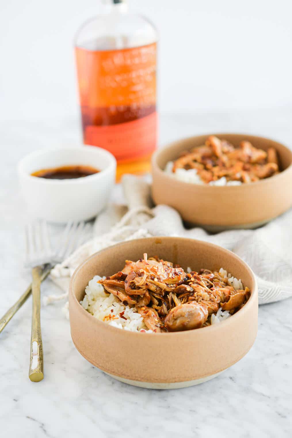 two beige bowls filled with white rice and bourbon chicken in front of a bottle of bourbon on a marble surface