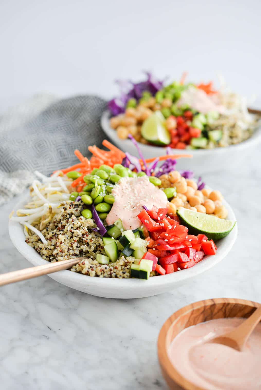 the side view of two thai red curry buddha bowls filled with quinoa, colorful veggies, and a creamy red sauce sitting on a marble surface