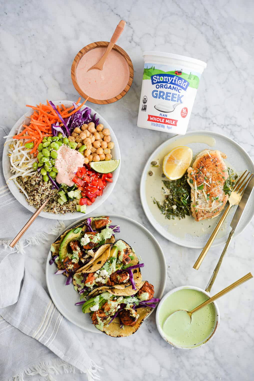 the top view of a thai red curry buddha bowl, three shrimp tacos, and a plate of creamy chicken piccata all surrounding a quart of Stonyfield's plain greek yogurt