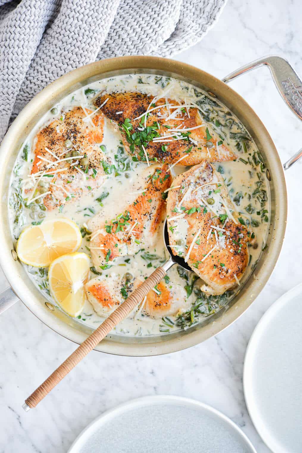 the top view of a skillet of creamy chicken piccata sprinkled with parmesan cheese on a marble surface