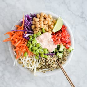 the top view of a thai red curry buddha bowl filled with quinoa, colorful, raw veggies, and a dollop of creamy yogurt red curry sauce on top, all sitting on a marble surface