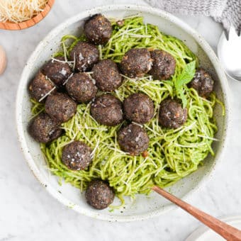 the top view of a bowl of pesto noodles topped with pesto meatballs sitting on a marble surface