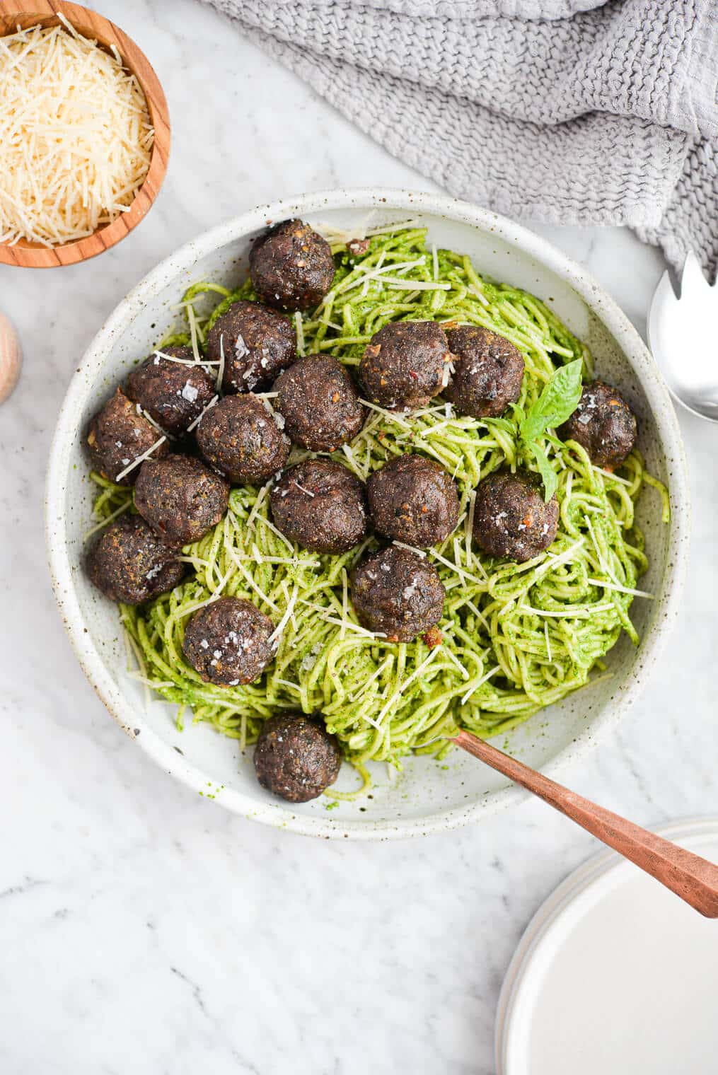 the top view of a bowl of pesto noodles topped with pesto meatballs sitting on a marble surface
