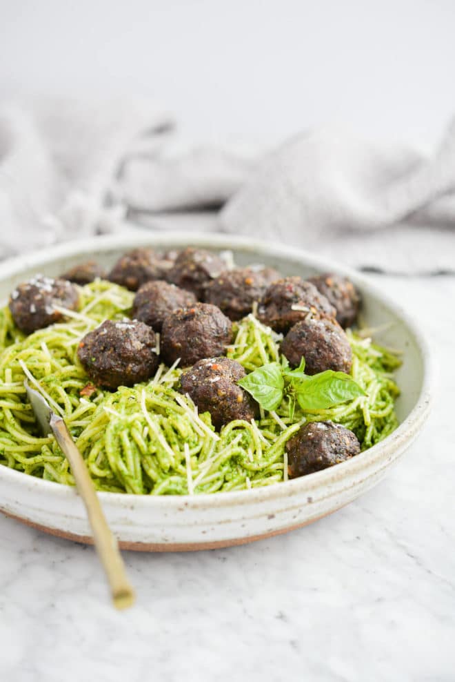 the side view of a bowl of pesto noodles topped with pesto meatballs sitting on a marble surface