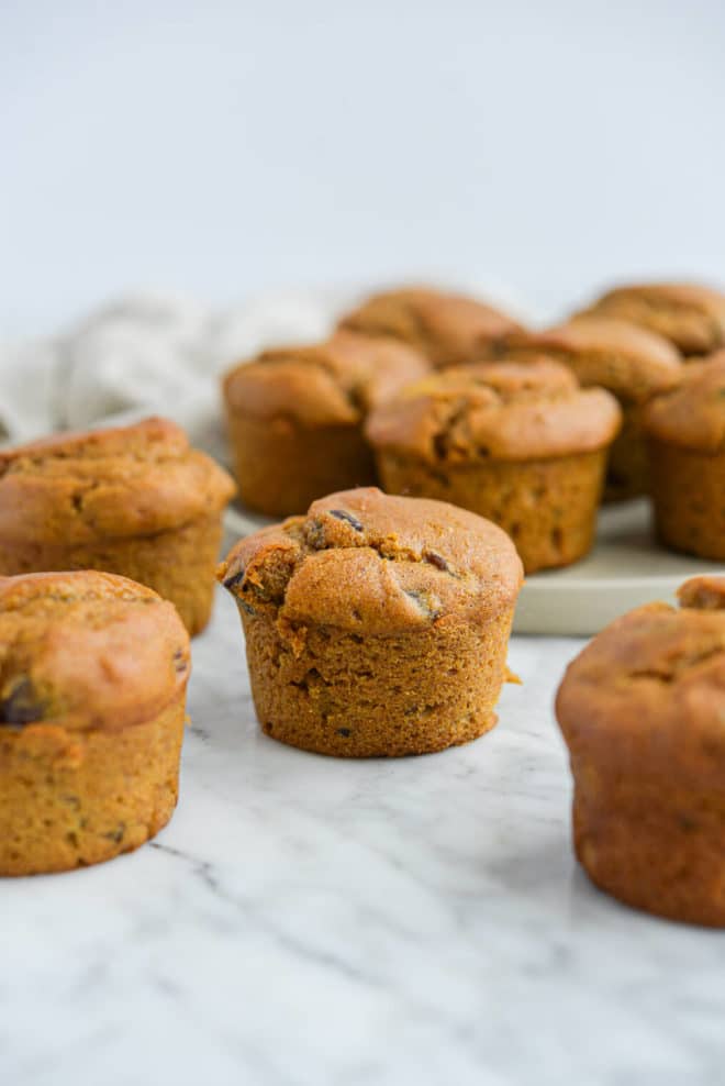the side view of 10 pumpkin chocolate chip muffins all sitting on a marble surface