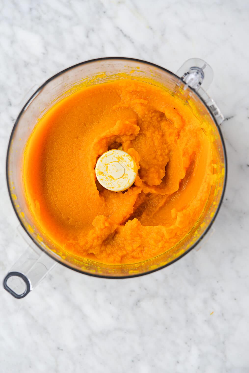 the top view of homemade pumpkin puree in an open food processor sitting on a marble surface