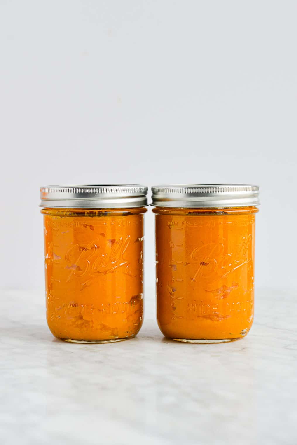 the side view of two lidded mason jars filled with homemade pumpkin puree sitting on a marble surface