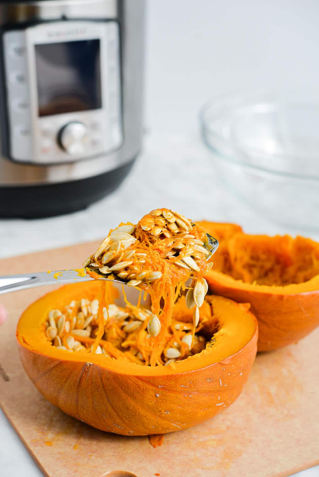 a side view of two halves of a cooked pumpkin with a blunt-nose spoon scooping out the pumpkin seeds
