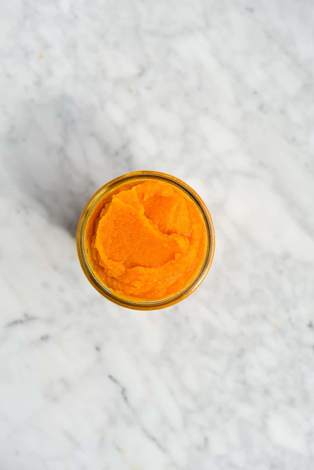the top view of an open mason jar filled to the top with homemade pumpkin puree sitting on a marble surface