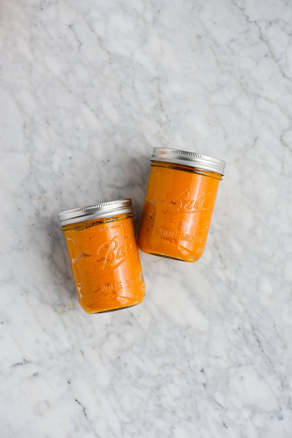 the top view of two lidded mason jars filled with homemade pumpkin puree and laying on their side on a marble surface