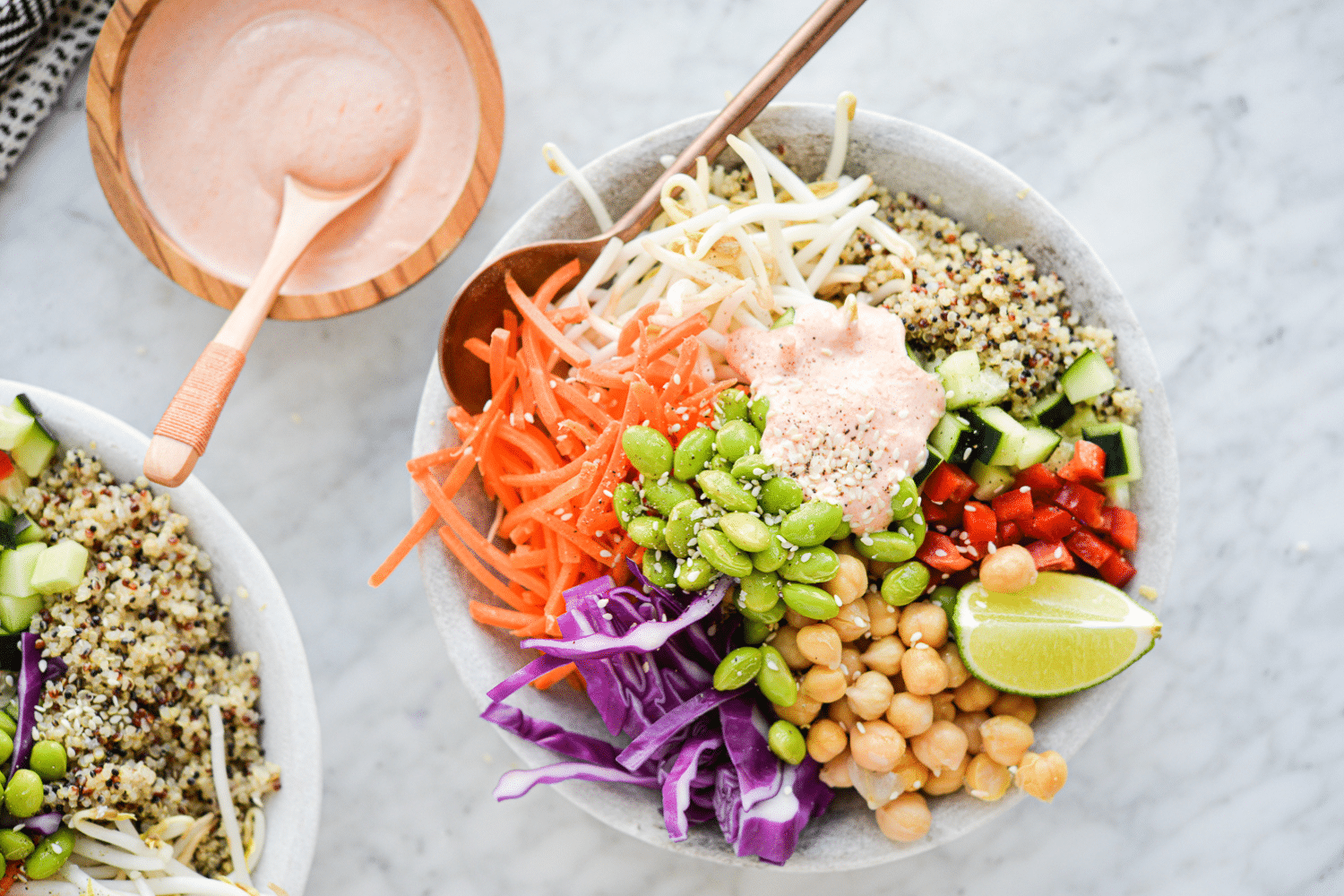 a close up of a thai red curry buddha bowl filled with quinoa, colorful, raw veggies, and a dollop of creamy yogurt red curry sauce on top, all sitting on a marble surface
