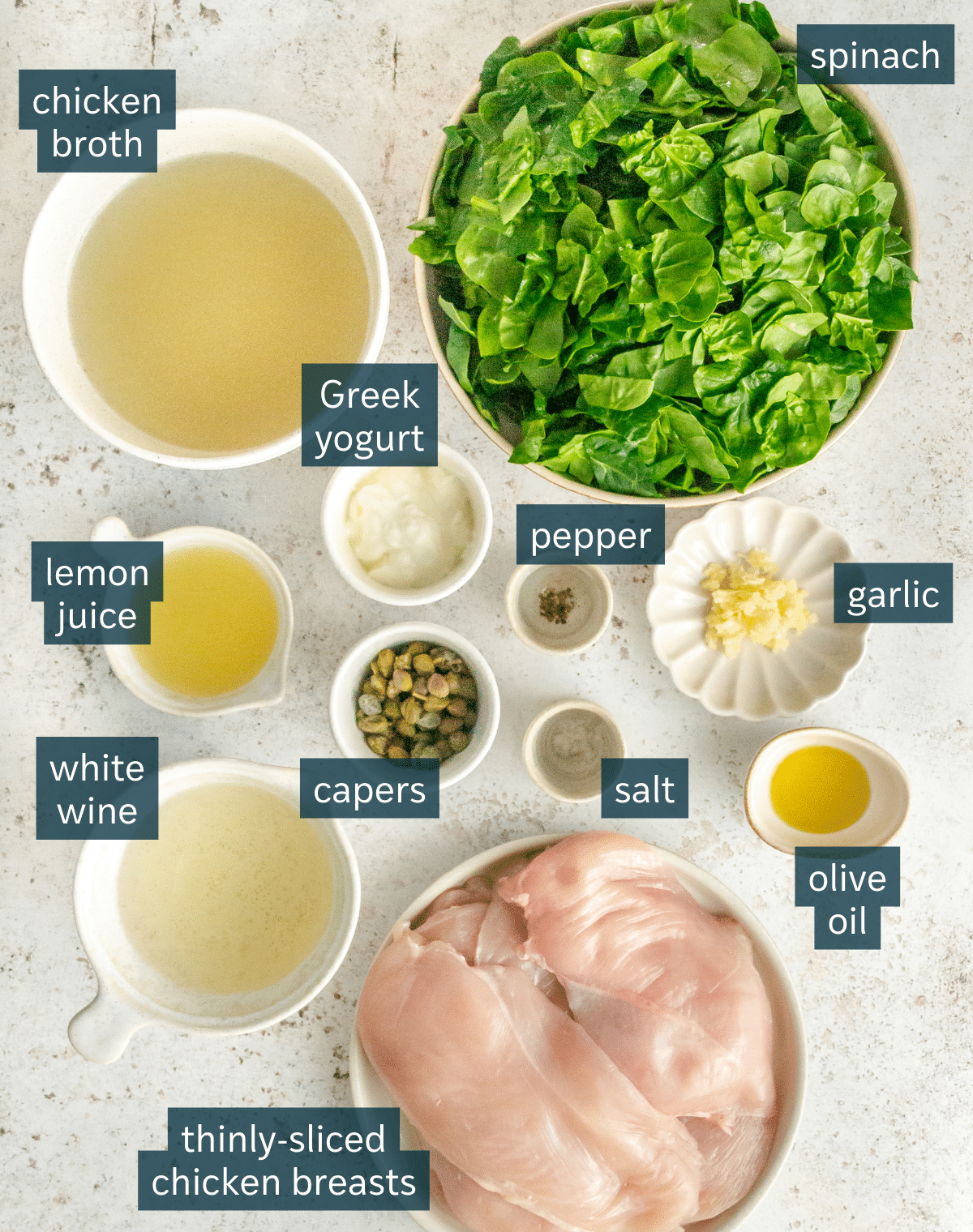 All of the ingredients needed for a creamy chicken piccata skillet in different sized bowls and plates on a light gray surface.