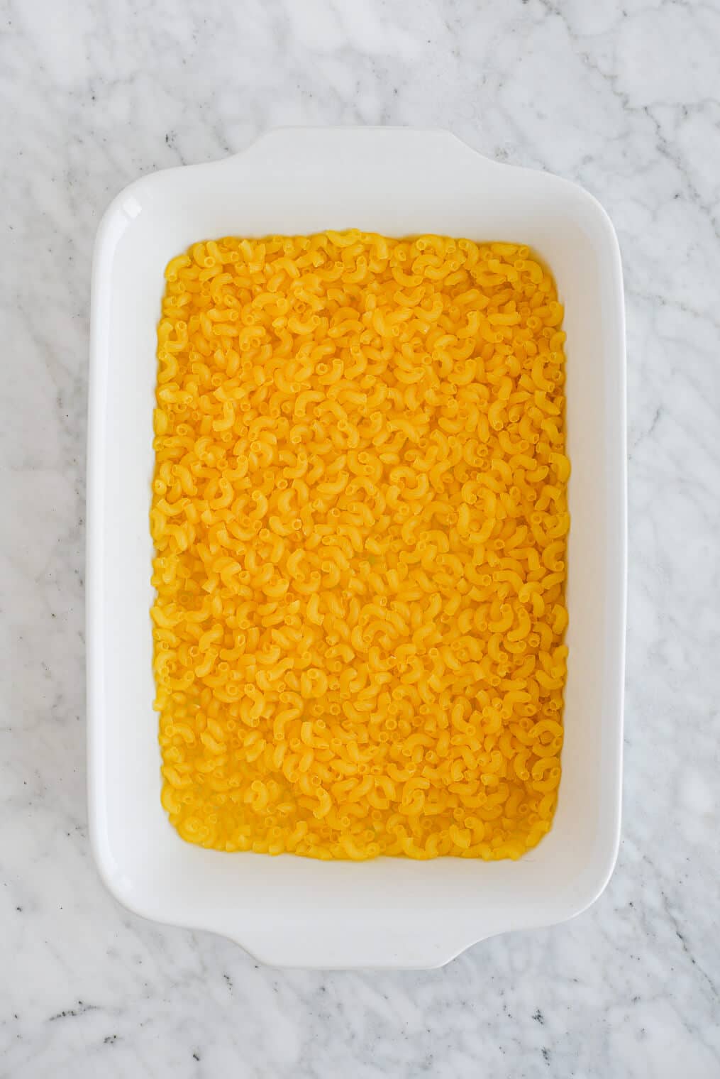 the top view of a casserole dish filled with uncooked macaroni noodles sitting on a marble surface
