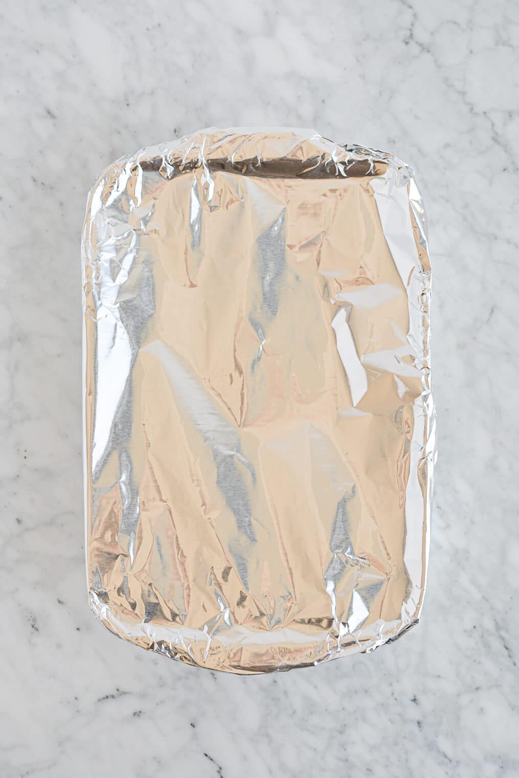 the top view of a foil covered casserole dish sitting on a marble surface
