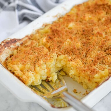 the side view of a casserole dish of oven-baked mac and cheese with one serving removed and a serving spoon scooping out another serving