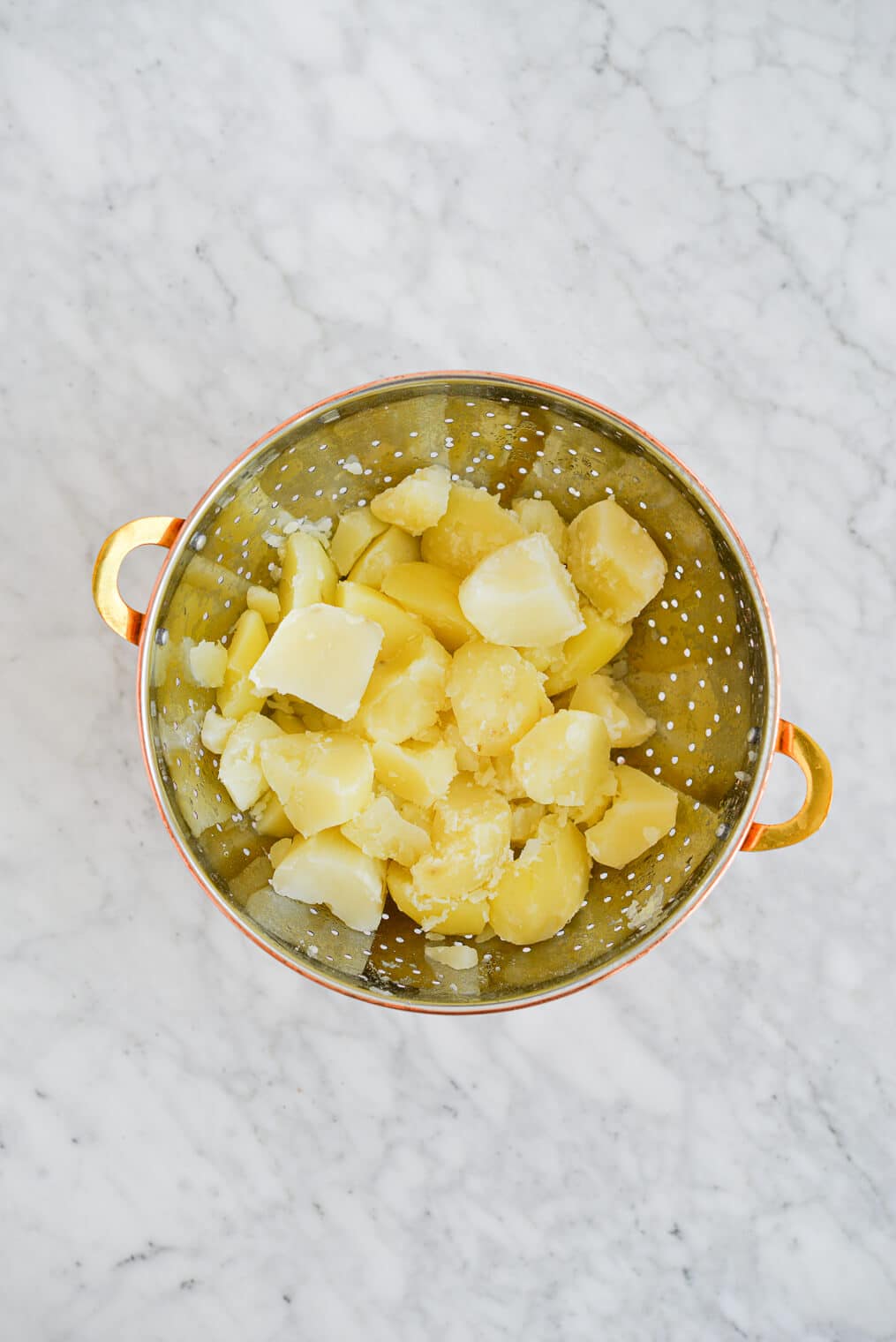 chopped and boiled potatoes in a strainer on a marble surface