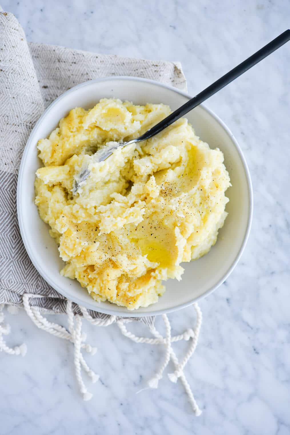 top view of a bowl of ready-to-eat mashed potatoes with a serving spoon sitting on a marble surface