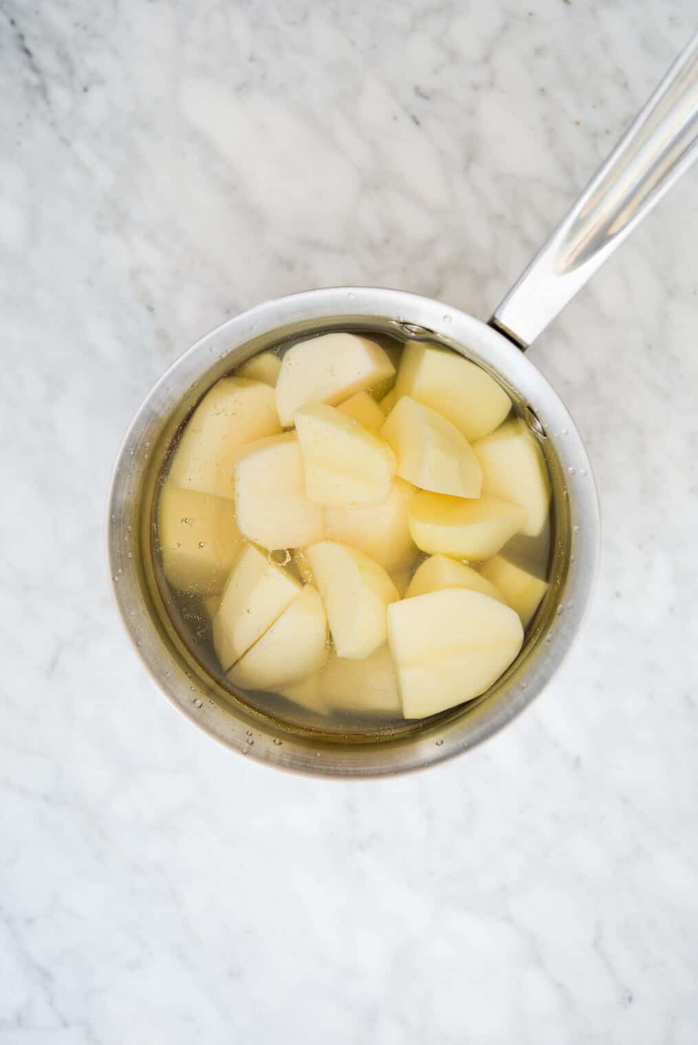 top view of a pot of water with chopped potatoes in it sitting on a marble surface