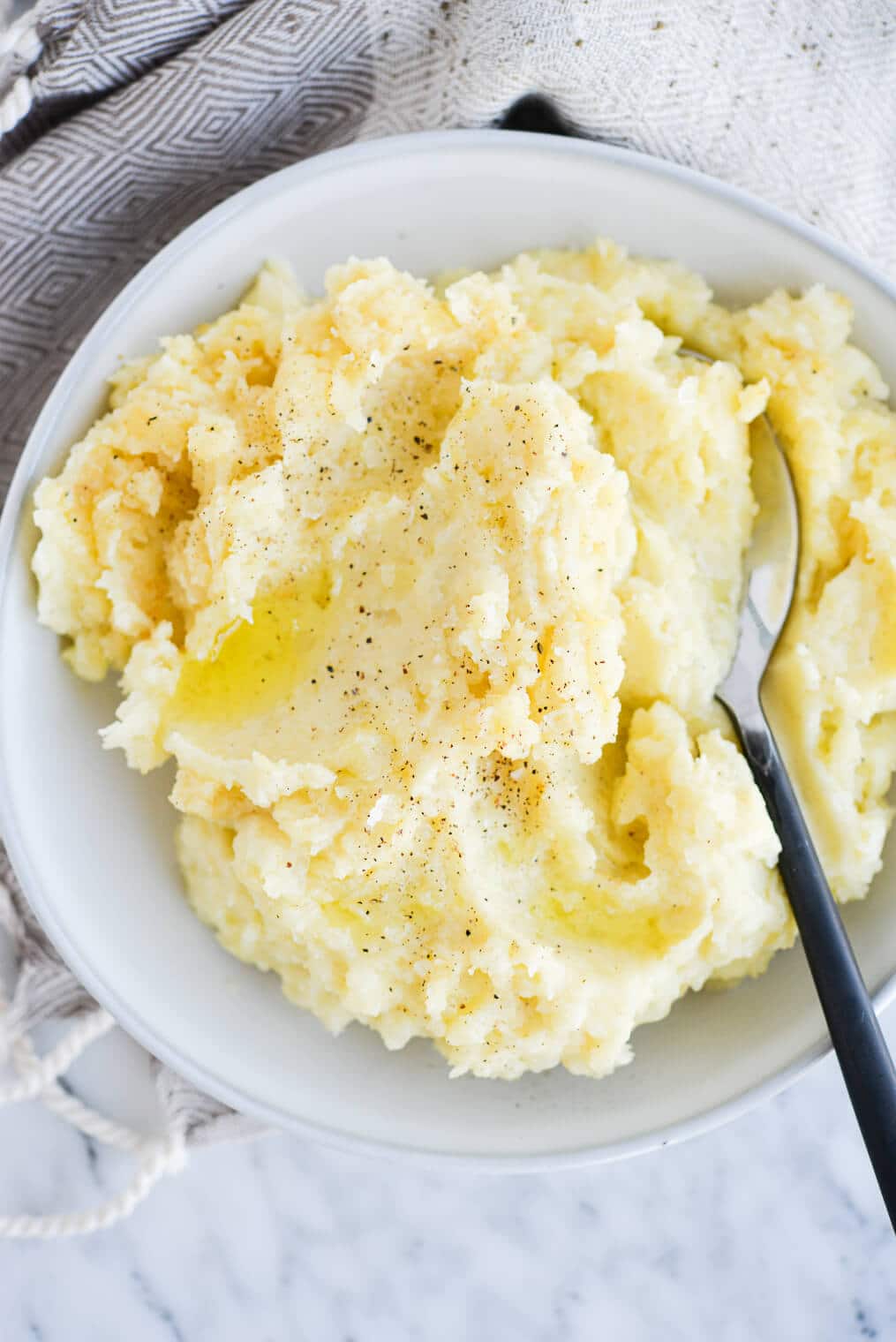 top view of a bowl of ready-to-eat mashed potatoes with a serving spoon sitting on a marble surface