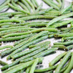 side view of roasted green beans on a sheet pan sitting on a marble surface