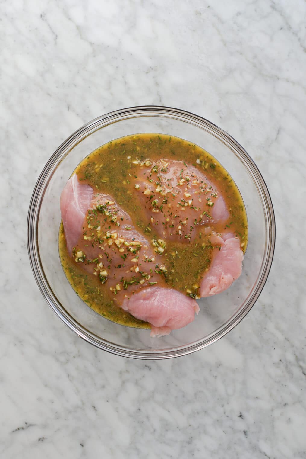 two turkey breast tenderloins marinating in a herb marinade in a glass bowl