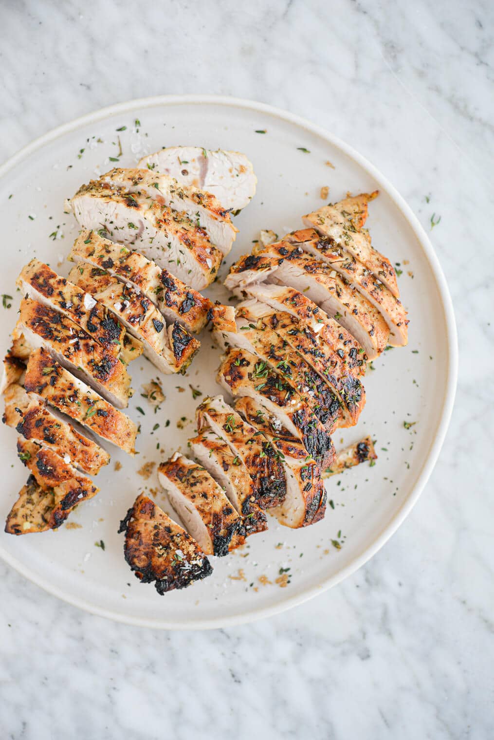 top view of two sliced turkey breast tenderloins sitting on a white plate on a marble surface