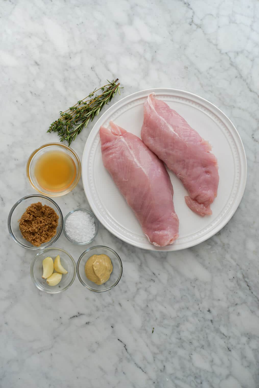 top view of two raw turkey breast tenderloins and all of the marinade ingredients sitting on a marble surface