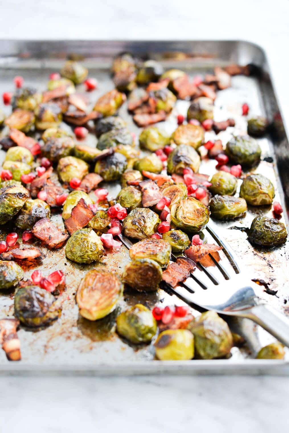 side view of roasted brussels sprouts, pomegranate seeds, and bacon on a sheet pan