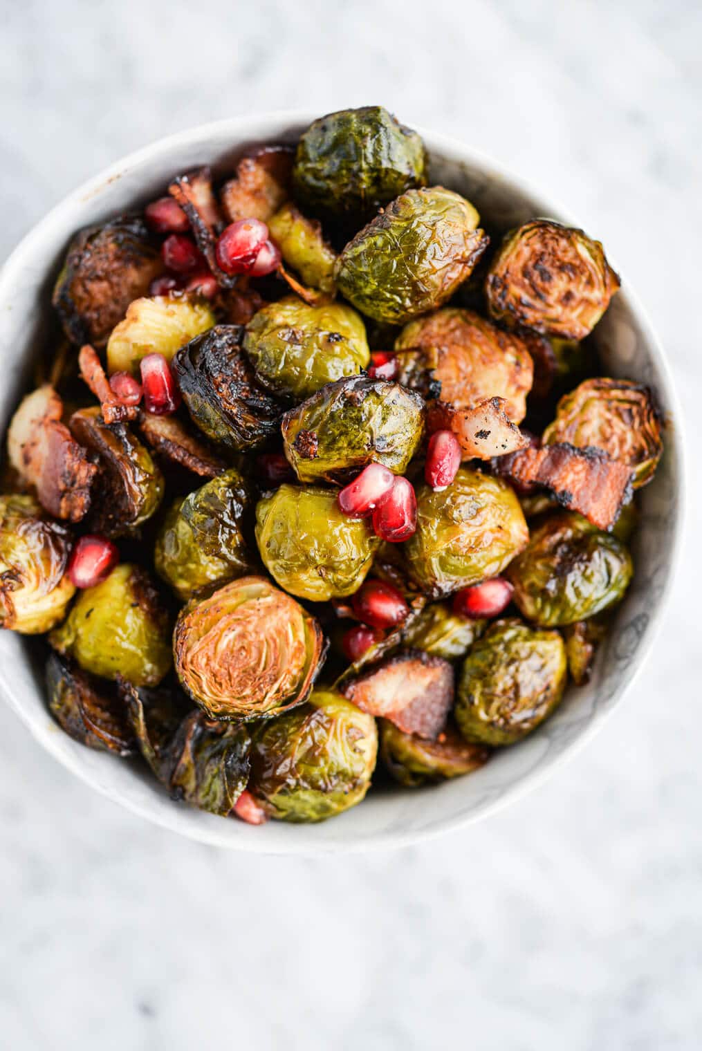 top view of a bowl of roasted brussels sprouts, pomegranate seeds, and bacon in a marble bowl on a marble surface
