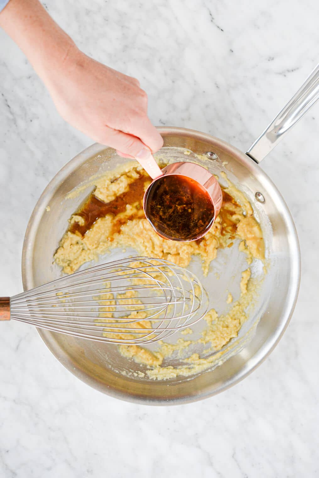 top view of a person pouring turkey stock into a pan of whisked flour and butter