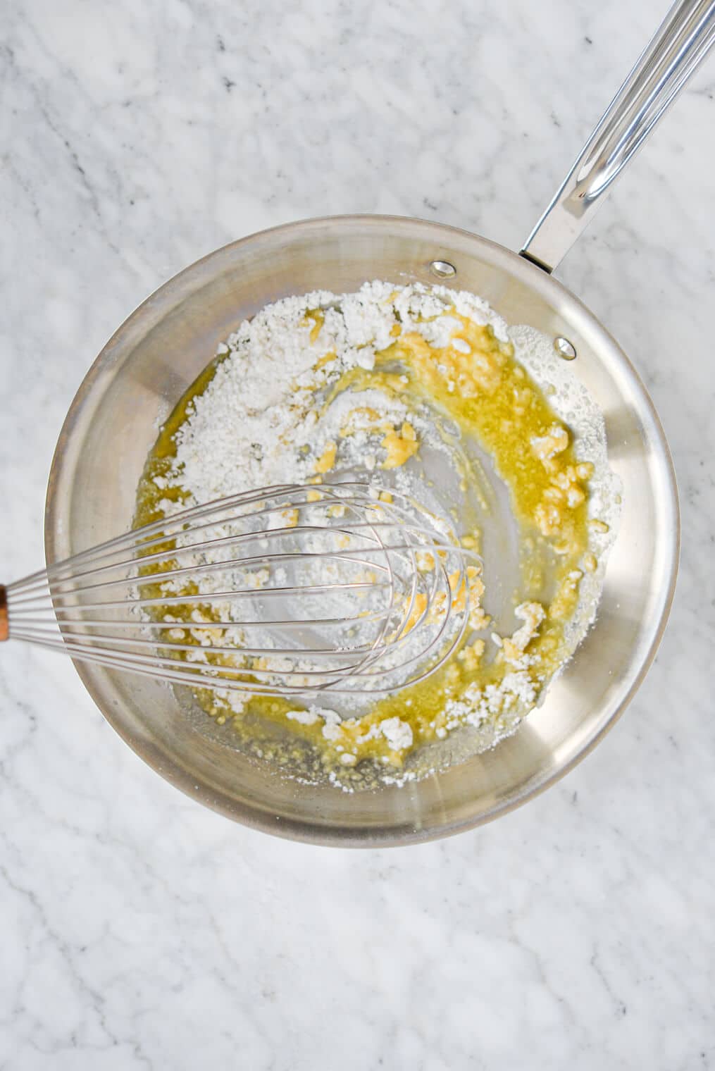 top view of flour being whisked into melted butter in a stainless steel pan