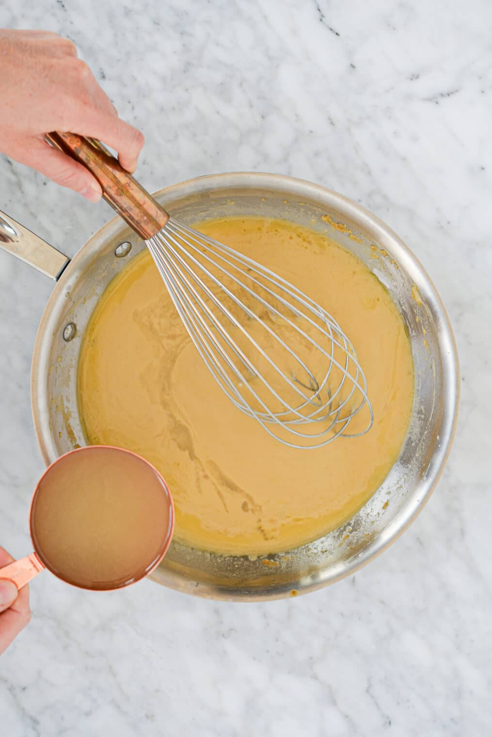 top view of chicken stock being whisked into butter and flour to make classic gravy